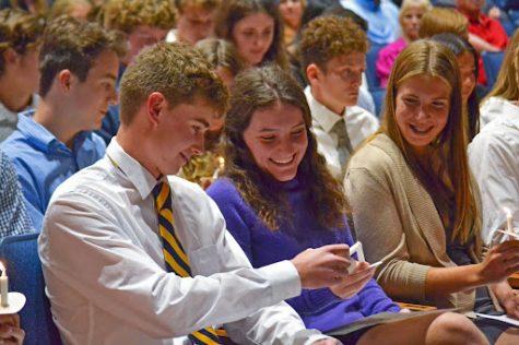 Laila Blumer (11) lights Noah Boyce’s (11) candle at the National Honor Society Induction ceremony on Oct. 10 in the auditorium while Floey Biteau (11) watches. Photo by: Maggie Murphy